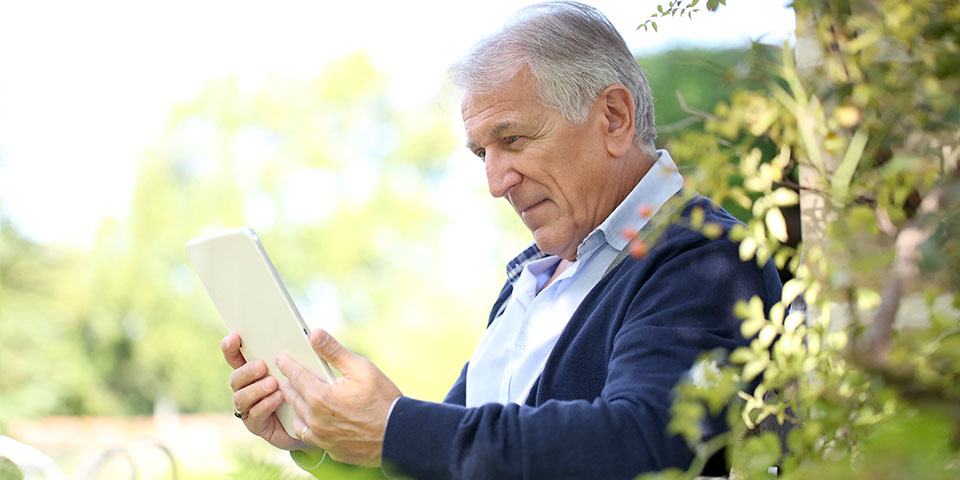 Älterer Mann sitzt auf Terrasse und liest auf einem Tablet